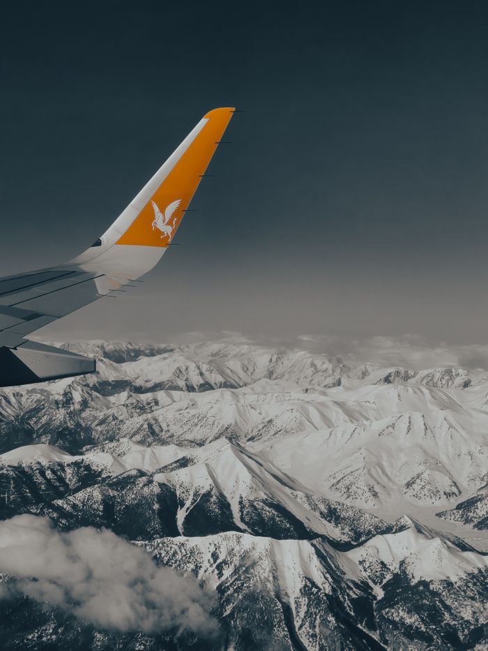 embark An airplane flies over snowcapped mountains, showcasing a serene aerial perspective.
