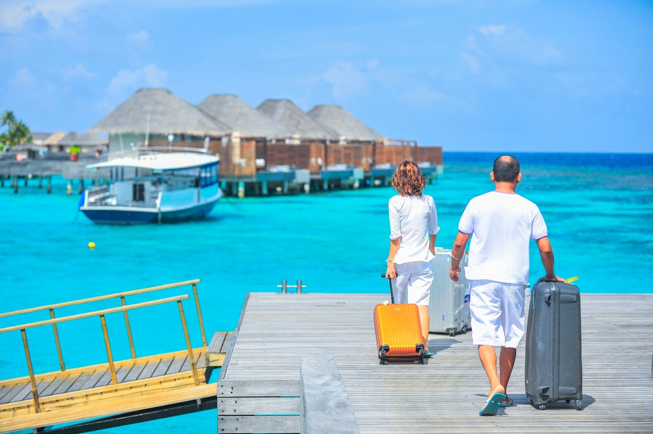 team-04 A couple arriving at a luxurious Maldives resort dock with luggage, capturing a tropical vacation vibe.