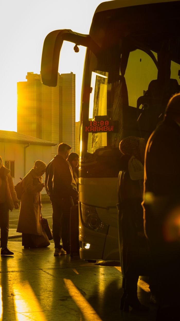 team-01 People boarding a bus in the city during sunset, creating a warm and inviting atmosphere.